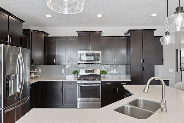 kitchen with appliances with stainless steel finishes, light countertops, dark brown cabinets, pendant lighting, and a sink