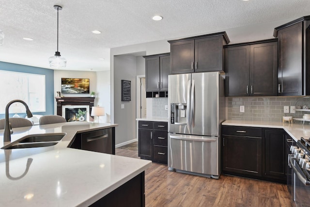 kitchen featuring dark wood finished floors, appliances with stainless steel finishes, hanging light fixtures, light countertops, and a sink