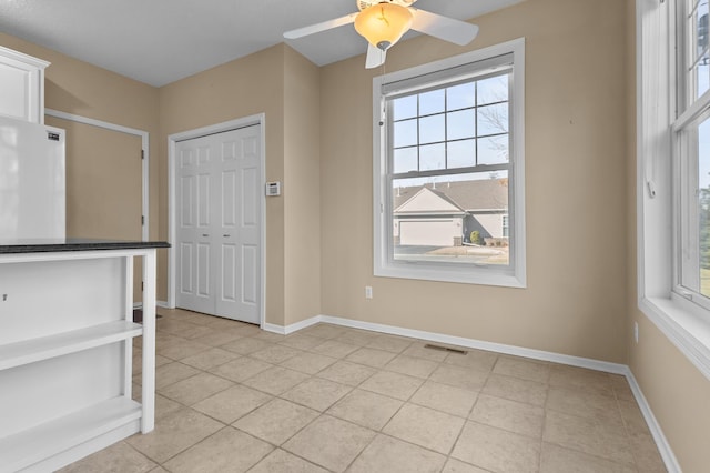 interior space featuring light tile patterned floors, ceiling fan, visible vents, and baseboards