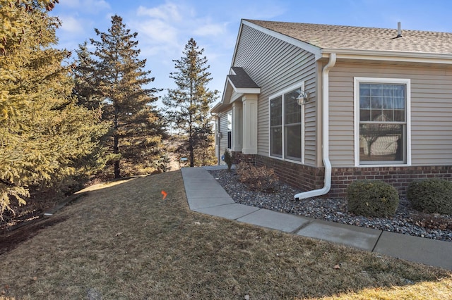 view of side of home with a shingled roof, brick siding, and a lawn