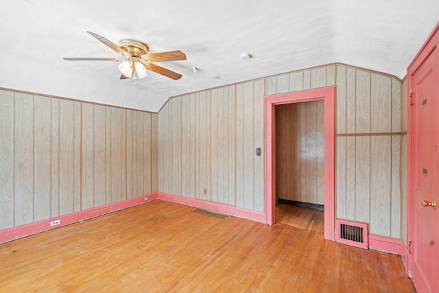 spare room featuring vaulted ceiling, wooden walls, and wood-type flooring