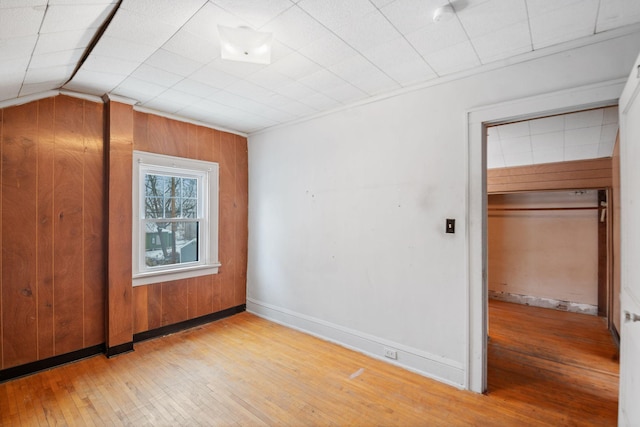 unfurnished bedroom with light hardwood / wood-style floors, a closet, and wood walls