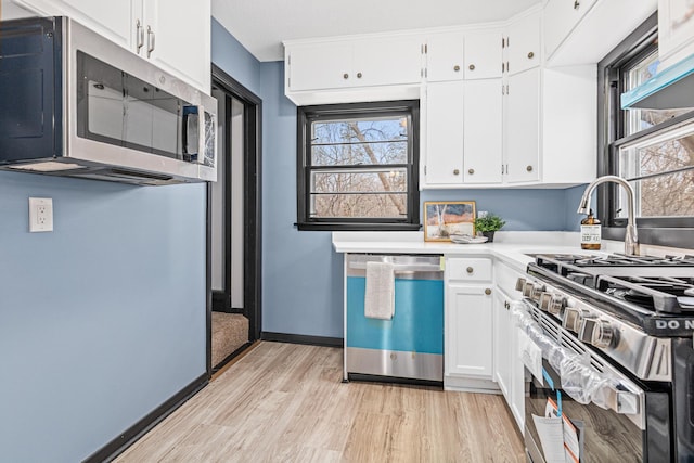 kitchen with appliances with stainless steel finishes, exhaust hood, white cabinets, and light hardwood / wood-style flooring