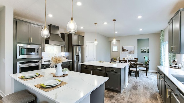 kitchen with a center island, appliances with stainless steel finishes, custom range hood, pendant lighting, and backsplash