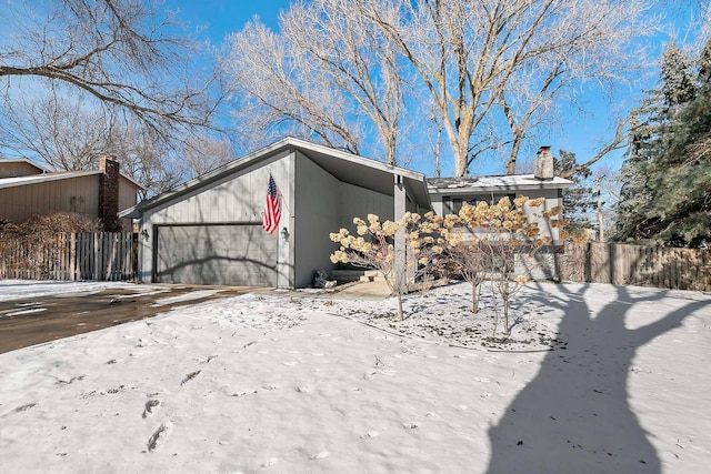 snow covered property with a chimney, fence, driveway, and an attached garage