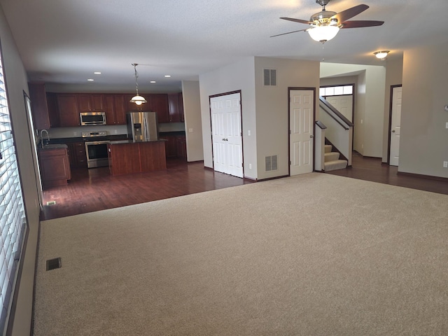 unfurnished living room with ceiling fan, sink, and dark colored carpet