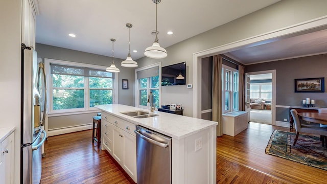 kitchen with sink, white cabinetry, hanging light fixtures, stainless steel appliances, and a kitchen island with sink