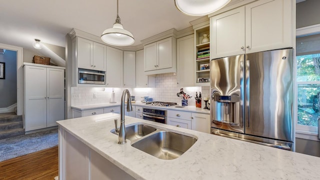 kitchen with sink, appliances with stainless steel finishes, pendant lighting, light stone countertops, and decorative backsplash