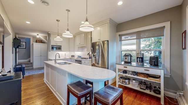 kitchen with sink, a kitchen breakfast bar, hardwood / wood-style flooring, hanging light fixtures, and stainless steel appliances