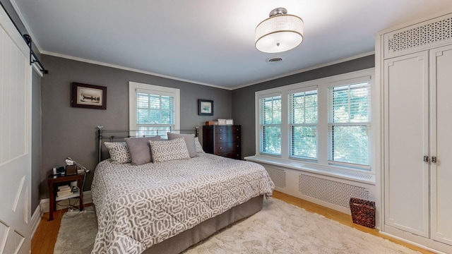 bedroom featuring radiator, crown molding, light hardwood / wood-style flooring, and a barn door