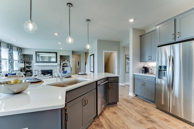 kitchen with appliances with stainless steel finishes, a stone fireplace, pendant lighting, sink, and light stone countertops