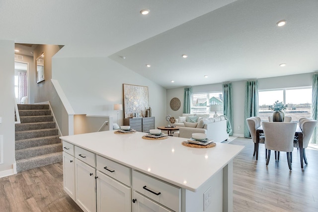 kitchen with lofted ceiling, a kitchen island, white cabinets, and light hardwood / wood-style floors