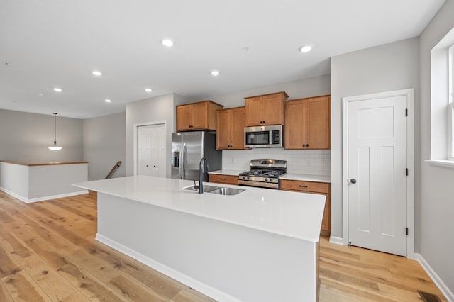 kitchen with stainless steel appliances, sink, a center island with sink, and decorative light fixtures