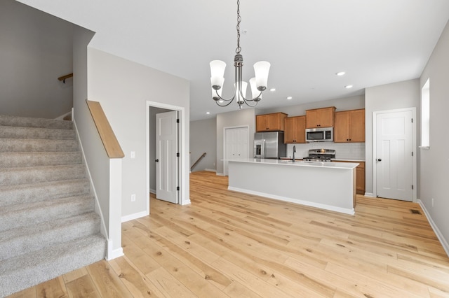 kitchen featuring sink, hanging light fixtures, an island with sink, stainless steel appliances, and light hardwood / wood-style floors