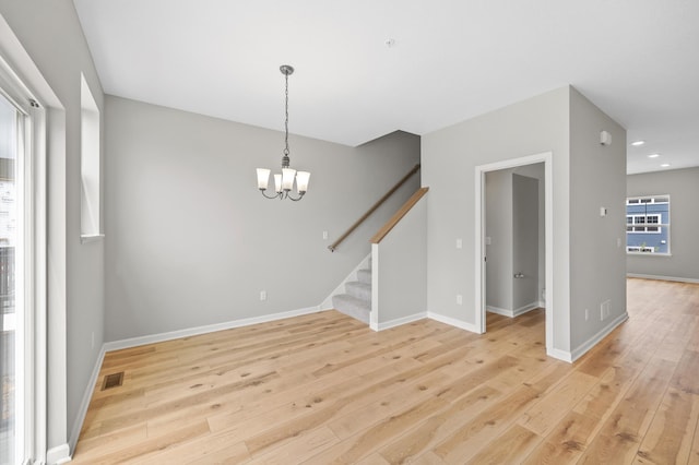 empty room with a notable chandelier and light hardwood / wood-style floors