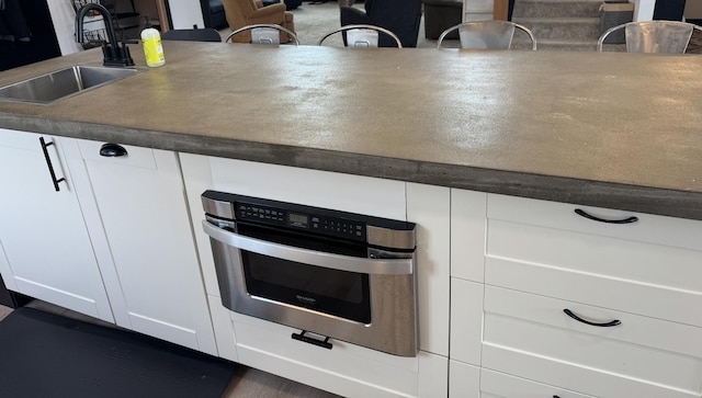 kitchen with white cabinetry, oven, and sink