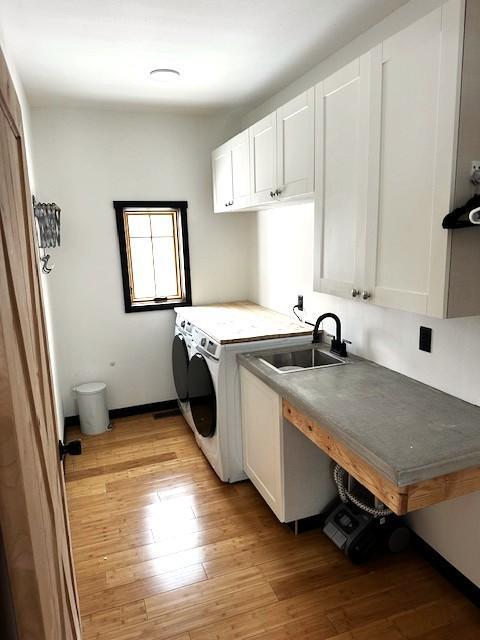 laundry room with cabinets, sink, light wood-type flooring, and washing machine and clothes dryer