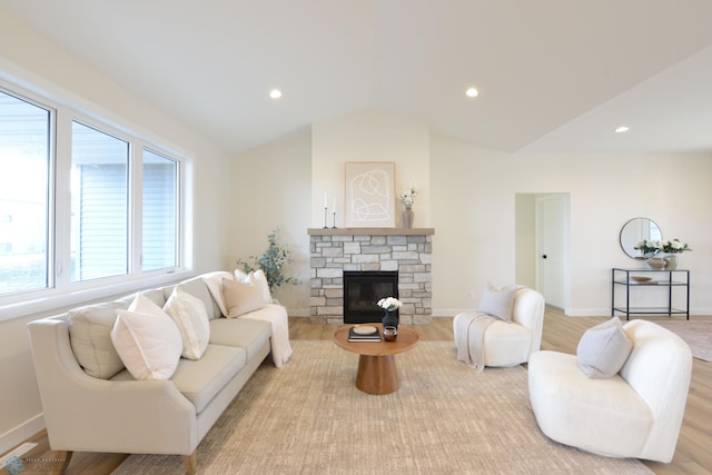 living area featuring lofted ceiling, light wood-style flooring, a stone fireplace, and recessed lighting