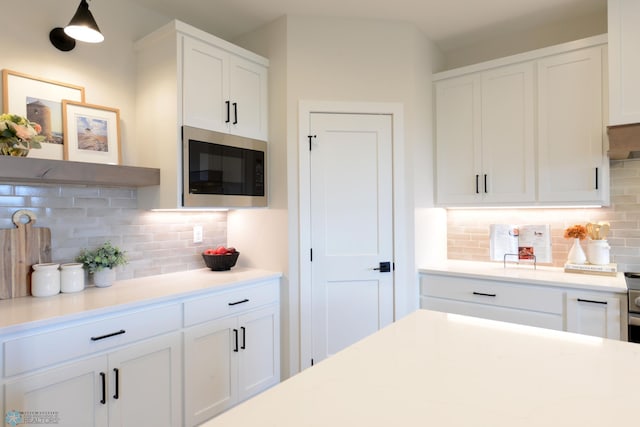 kitchen with stainless steel microwave, backsplash, light countertops, and white cabinets