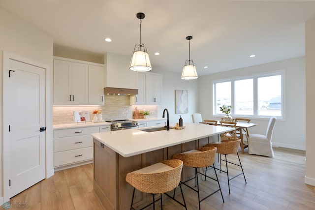 kitchen featuring stainless steel electric stove, a sink, light wood-type flooring, decorative backsplash, and an island with sink