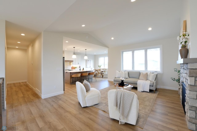 living area with light wood-style flooring, a fireplace, baseboards, lofted ceiling, and recessed lighting