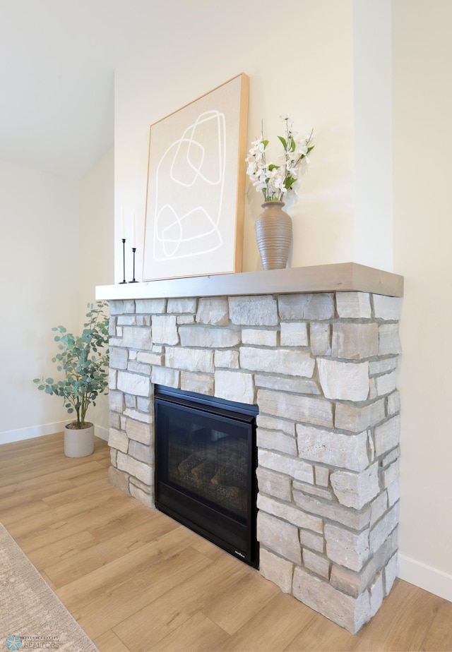 details with baseboards, wood finished floors, and a stone fireplace
