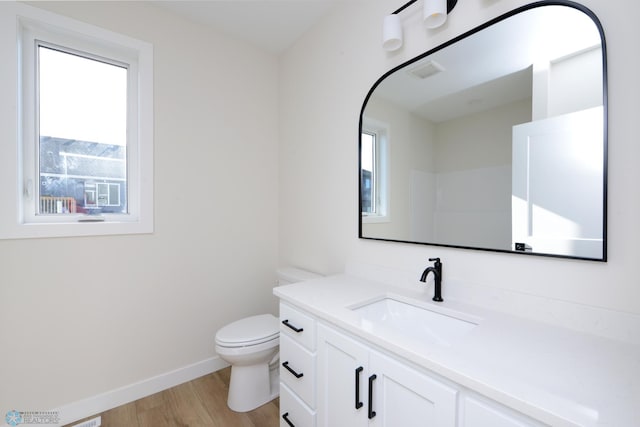 bathroom with toilet, visible vents, baseboards, wood finished floors, and vanity