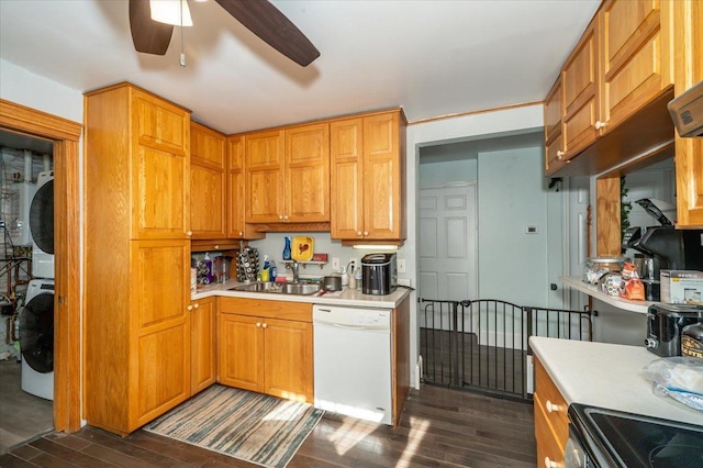 kitchen with white dishwasher, stacked washing machine and dryer, a sink, dark wood-style flooring, and a ceiling fan