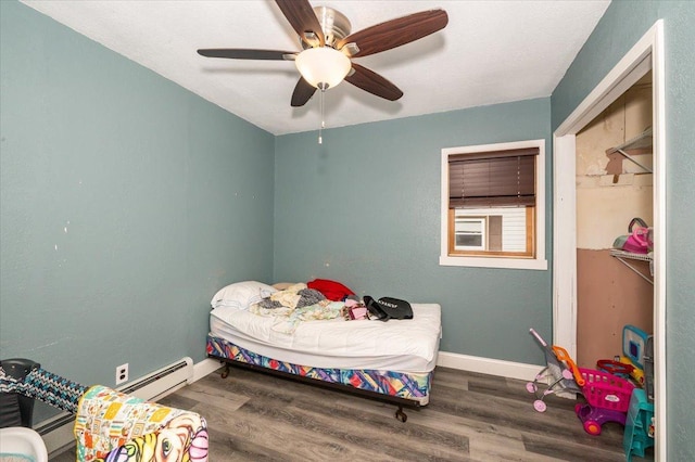 bedroom with a baseboard heating unit, wood finished floors, and baseboards