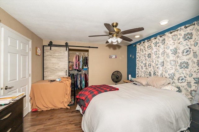 bedroom with wood finished floors, a barn door, a closet, a ceiling fan, and a spacious closet