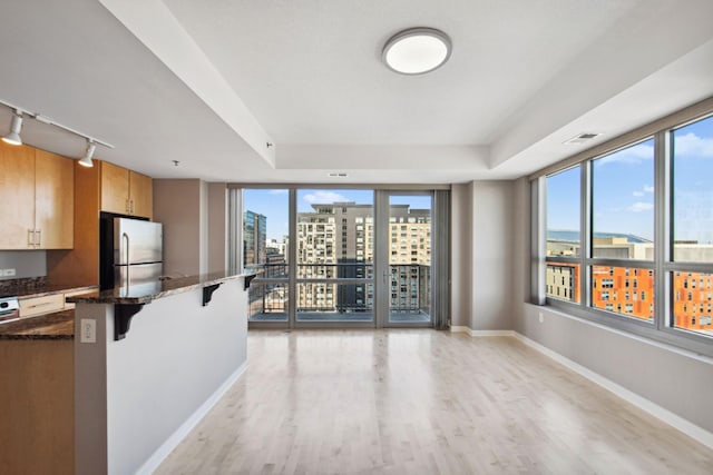 kitchen featuring a breakfast bar, a view of city, brown cabinets, freestanding refrigerator, and dark stone counters