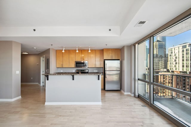 kitchen with light wood finished floors, baseboards, a breakfast bar area, a view of city, and stainless steel appliances