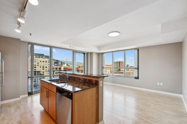 kitchen featuring a kitchen island with sink, a city view, light wood-style floors, dishwasher, and brown cabinetry