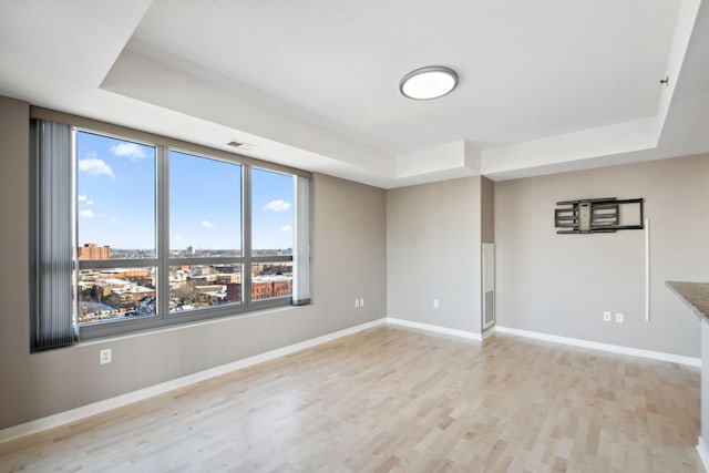 empty room with light wood-style floors, a raised ceiling, visible vents, and baseboards