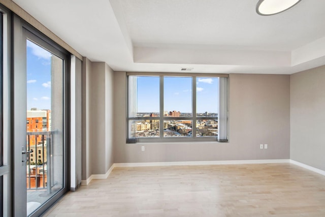 unfurnished room with light wood-type flooring, a raised ceiling, and baseboards