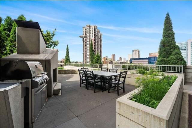 view of patio / terrace featuring a view of city, outdoor dining space, an outdoor kitchen, and a grill