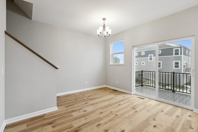 empty room featuring a notable chandelier and light wood-type flooring