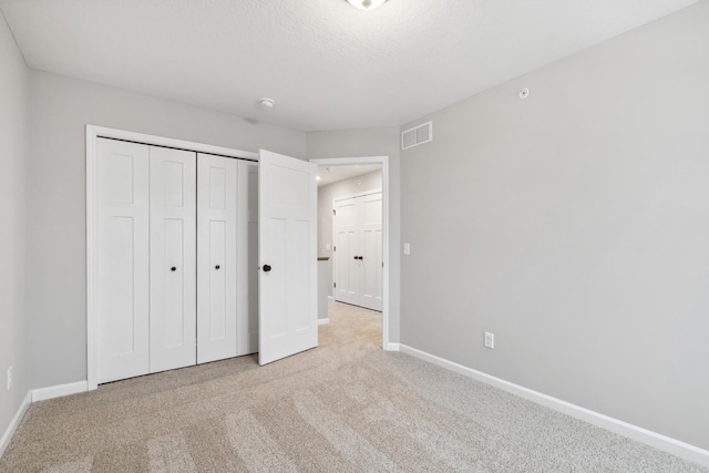 unfurnished bedroom featuring light carpet, a closet, and a textured ceiling