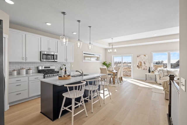 kitchen featuring hanging light fixtures, an island with sink, stainless steel appliances, light hardwood / wood-style floors, and white cabinets