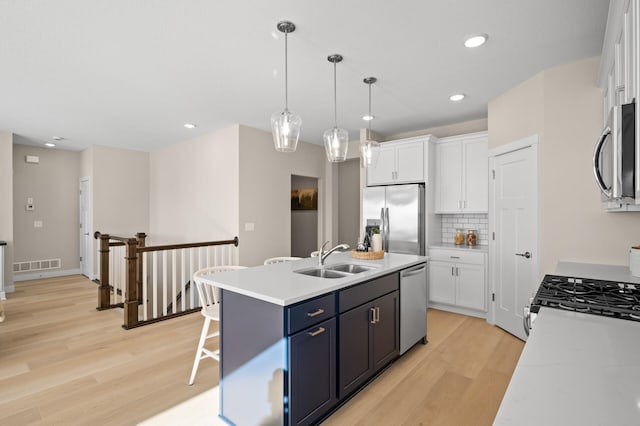 kitchen featuring sink, white cabinetry, decorative light fixtures, a center island with sink, and stainless steel appliances