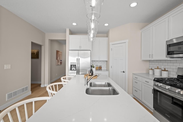 kitchen with stainless steel appliances, sink, white cabinets, and decorative light fixtures