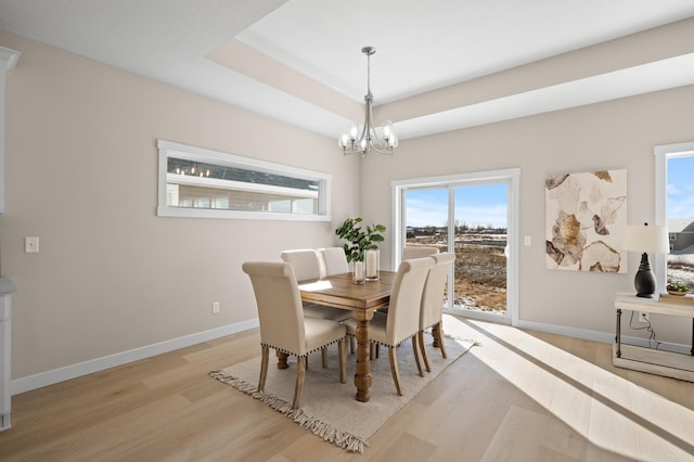 dining space with an inviting chandelier, light hardwood / wood-style floors, and a raised ceiling