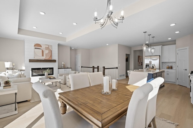 dining area featuring a fireplace, sink, light hardwood / wood-style floors, a tray ceiling, and an inviting chandelier