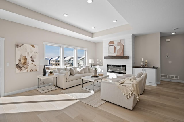 living room featuring a tray ceiling, a fireplace, and light hardwood / wood-style floors