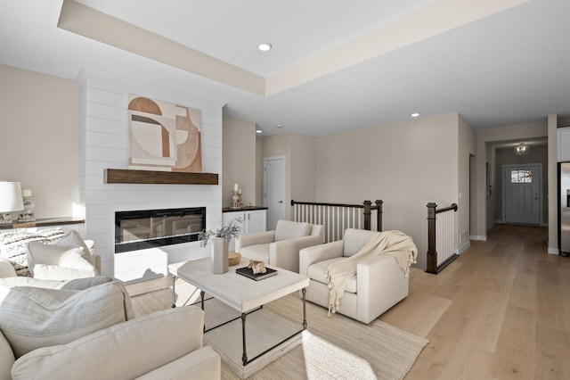 living room with a tray ceiling, a fireplace, and light wood-type flooring