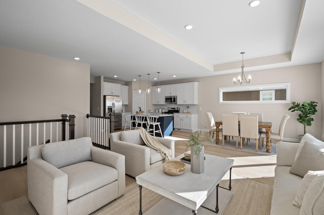 living room with a notable chandelier, light wood-type flooring, and a tray ceiling