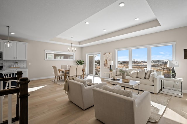 living room with a tray ceiling, a chandelier, and light wood-type flooring