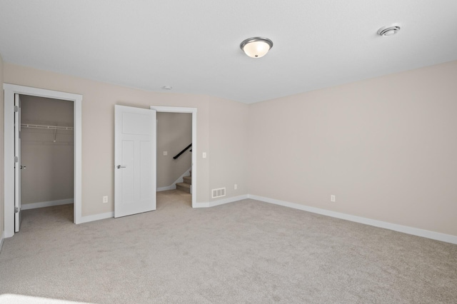 unfurnished bedroom featuring a spacious closet, light colored carpet, and a closet