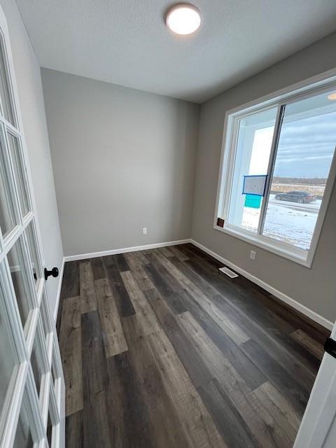 spare room with baseboards, dark wood finished floors, and a textured ceiling