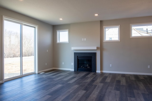 unfurnished living room featuring baseboards, dark wood finished floors, and a wealth of natural light